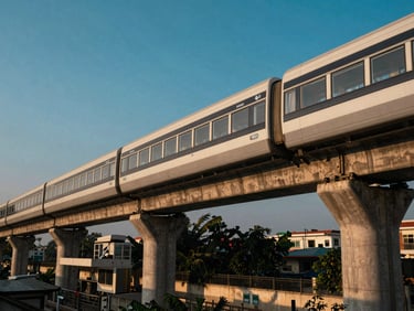Wide environmental shot of a modern elevated metro rail system in Dhaka during golden hour, clean architectural lines.