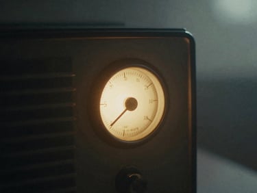 Close-up of a vintage radio dial glowing softly in a dark room, warm amber light, heavy shadows, 35mm grain