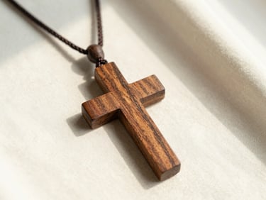 Close-up of a dark walnut wood cross necklace on soft cream fabric, gentle morning light