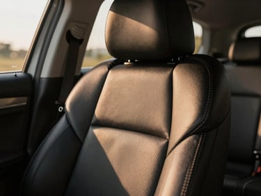 Macro close-up of premium hand-stitched black leather seats inside a modern luxury vehicle, warm golden sunlight streaming through the window highlighting the immaculate texture.