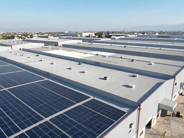 Aerial drone shot of a massive industrial warehouse in Tijuana, covered in modern solar panels under bright high-contrast desert sunlight, crisp shadows.