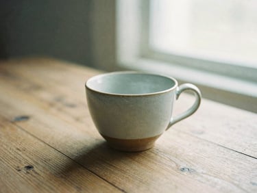 An empty ceramic cup on a rustic wooden table, soft diffused morning light casting long shadows