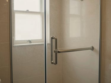 Medium shot of a modern bathroom with a newly installed level-access walk-in shower, soft natural daylight filtering through a window, elegant textured tiles, matte metal grab bar, high-contrast warm tones, 35mm.