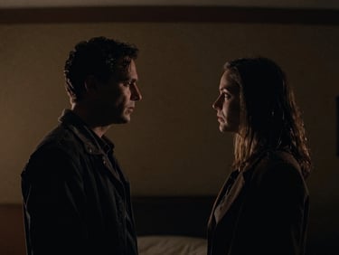 Widescreen cinematic still from a narrative film, two characters in a dramatic moment, high-contrast chiaroscuro lighting, deep shadows, warm moody tones, anamorphic lens, 35mm grain.
