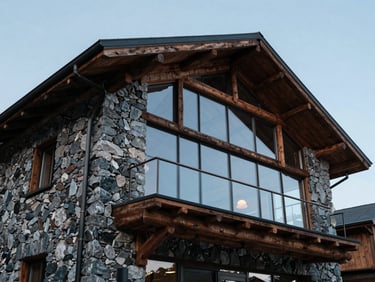 Low-angle hero shot of a modern mountain lodge, raw iron-ore stone walls, heavy timber beams, massive glass panels under cold light.