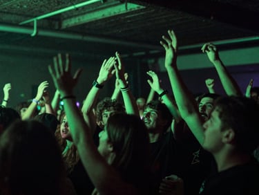 Wide low-angle shot of an underground trap concert, crowd hands raised, high-contrast neon green lighting, raw energy, 35mm film
