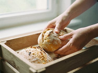 Close-up detail of hands placing fresh bread and warm soup into a rustic wooden crate, soft natural window light, 35mm film.