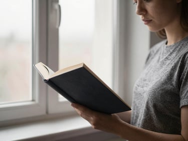 Focused adult learner reading a dense hardcover book, directional window light, 50mm lens.
