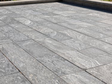 Detail shot of a completed paver patio in natural daylight — tight-fitted coastal gray stone pavers with clean jointing, low retaining wall edge visible, no people