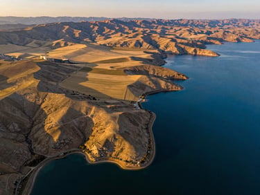 Sweeping wide drone photography of premium land plots on the shores of Lake Van, Turkey, golden hour lighting highlighting the topography, deep blue water contrasting with golden fields, cinematic 16:9 crop.