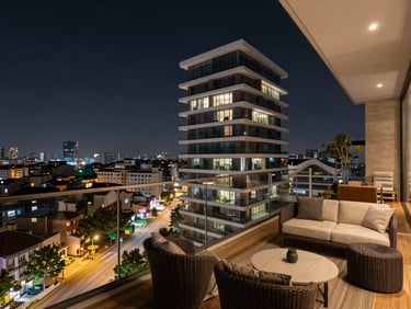 Şık penthouse dairesinin çatı terası, modern dış mekan mobilyaları, şehir manzaralı cam korkuluklar, loş akşam aydınlatması.