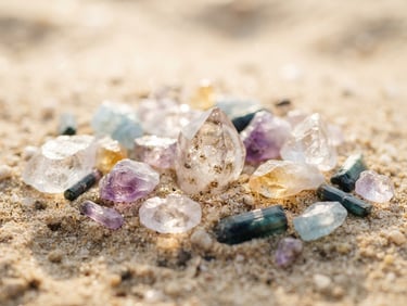 Luminous editorial photography of raw, light-catching semi-precious stones resting on a warm sand surface, soft morning daylight, macro lens, shallow depth of field