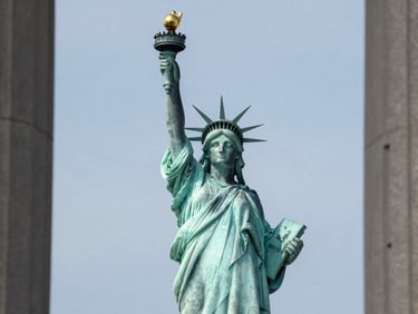 Statue of Liberty photographed frontally in bright even daylight, clear sky, clean architectural framing, no dramatic lighting, calm institutional tone