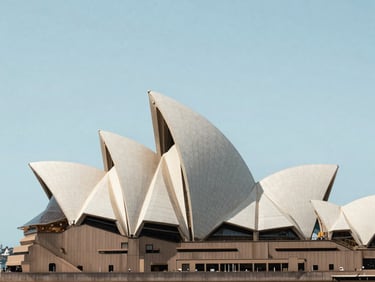 Sydney Opera House roof shells photographed frontally in bright even daylight, harbour in background, clean sky, architectural framing, calm institutional light