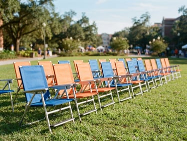A neat alignment of premium blue and orange portable folding chairs set up on a sunlit lawn in Gainesville, bright natural light, 35mm lens