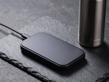 Matte black wireless charger and sleek thermal bottle on textured slate, dramatic side lighting.