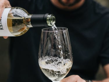 Close-up of a hand pouring a pale white wine into a glass, showcasing a clean, modern label on the bottle.