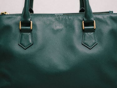 Close-up of structured leather stitching on a dark green handbag, soft shadows, overcast daylight, editorial film photography, 35mm