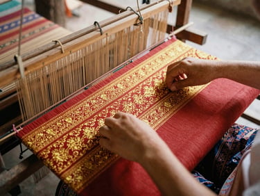Hands of a Thai weaver working on a traditional wooden loom, intricate gold and red silk patterns
