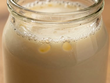 Bubbly active milk kefir fermenting in a glass jar, macro shot showing tiny gas bubbles and rich creamy texture, warm lighting.