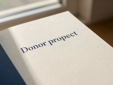 A close-up of a printed donor prospectus booklet with minimalist layout, elegant serif typography, matte paper texture, warm natural light.