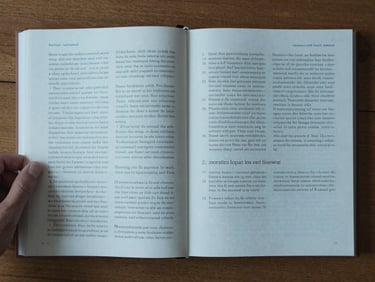 Overhead flat-lay of an open academic manuscript on a wooden desk, a hand resting beside annotated pages, cool north-facing daylight falling across the paper, dense margin notes visible in ink, no digital devices