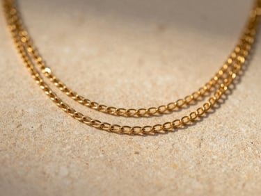 Macro close-up of three layered gold chains resting on warm natural stone, soft golden-hour side lighting, showing the solid sterling base texture