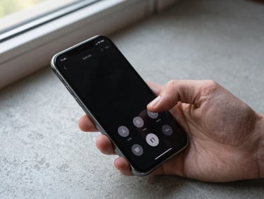 Close-up overhead shot of a hand holding a smartphone on a concrete surface, screen lit with a dialer, natural daylight from a nearby window, slight shadow from fingers