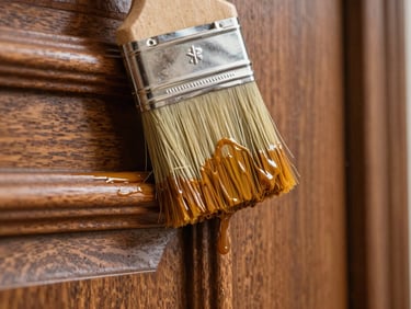 Extreme close-up of a professional paint brush applying a smooth coat of amber-gold protective varnish to a detailed wooden door panel, showing the rich grain.