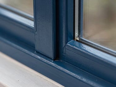 Close-up of the exact same wooden window frame joint, now perfectly repaired, sanded smooth, and finished with a flawless semi-gloss dark blue paint, sharp paint lines.