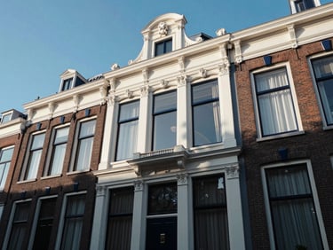 Wide heroic shot of a classic, beautifully maintained Dutch residential facade in Rotterdam, featuring immaculate white and navy blue exterior trim under a clear blue sky.