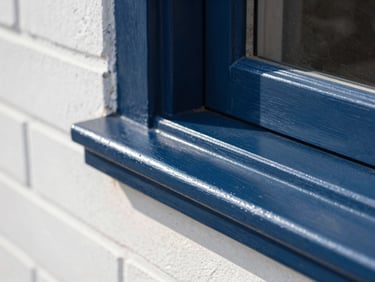 Extreme close-up of a wooden window frame painted in high-gloss navy blue, reflecting crisp morning sunlight, with razor-sharp paint lines against a clean white brick wall.