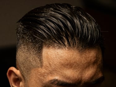 Macro shot of a perfectly executed hair fade on a man's head, sharp lines, dark hair against a dark background, low-key warm lighting, 35mm.