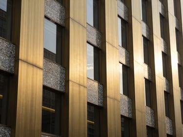 Tight abstract detail shot of a premium brushed brass and granite facade on a modern corporate headquarters, crisp morning light.