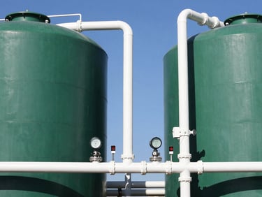 Two large green water storage tanks connected by clean PVC piping and automated electronic pump controllers, bright South African sun