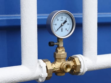 A mechanical pressure gauge and brass valve manifold on a water system, crisp focus, blue tones