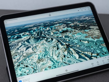 A close-up of a rugged tablet screen displaying 3D topographic contour lines and GIS shapefiles over a cool overcast landscape