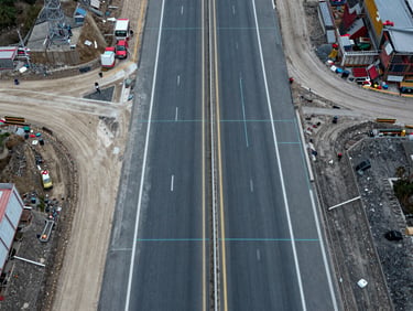Top-down nadir perspective of a highway construction site, sharp overcast lighting, crisp technical details with faint cyan vector grid lines
