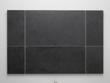 Minimalist bathroom wall featuring textured dark charcoal ceramic tiles, soft side lighting highlighting the relief.