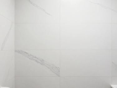 Minimalist bathroom interior with large-format white marble-look tiles, clean grout lines, bright neutral daylight, clean white and charcoal tones, sharp focus, 35mm lens