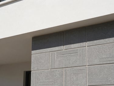 Close-up of textured charcoal elevation tiles on an exterior facade, geometric shadows, bright neutral daylight, clean white and charcoal tones, sharp focus, 35mm lens