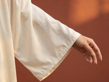 Close-up of a draped ivory silk robe sleeve, delicate hand-stitching visible, warm terracotta background, soft lighting