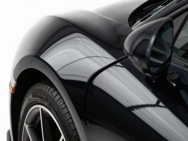 Extreme close-up of a high-end sports car fender, clinical white studio light reflecting sharp lines on deep black paint, macro detail, 50mm