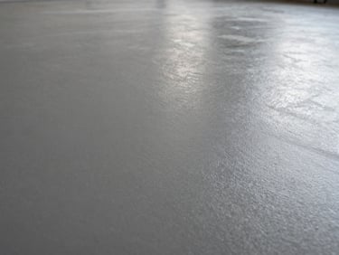 Extreme close-up 45-degree angle shot of a urethane resin floor surface in an industrial warehouse, showing fine texture and matte sheen under diffused overhead studio lighting, surface fills the entire frame, no shadows obscuring texture detail, no people