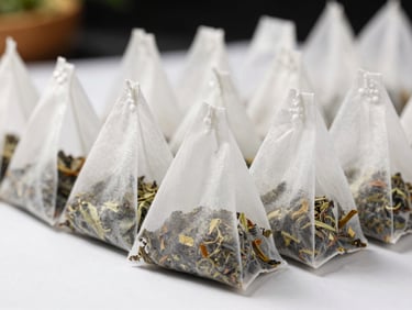 Close-up of uniform pyramid tea bags sealed in a row on a white production surface, dried herbal blend visible through mesh, bright studio lighting