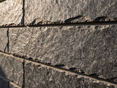 Macro detail shot of natural slate stone tiles on an exterior wall, textured surface, sharp architectural shadow