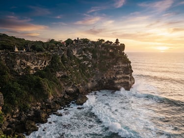 Dramatic limestone cliffs of Uluwatu at sunset, temple perched on the edge, golden-hour light hitting the ocean waves, 35mm lens.