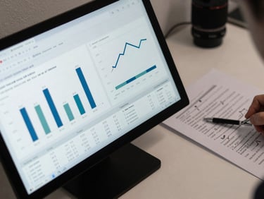 Tight overhead shot of a screen showing a data analysis dashboard with bar charts and regression tables, a printed results section beside it with pencil annotations, cool white desk light