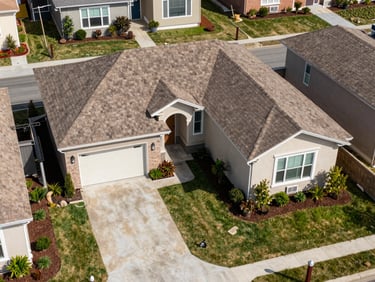Wide aerial view of a residential property listing showing roofline, driveway, and landscaping from directly above, natural daylight, no people, clean site conditions