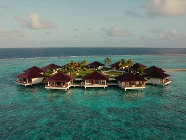 Vue aérienne d'une villa sur pilotis aux Maldives, eau turquoise, ciel clair. Ambiance de voyage de luxe.